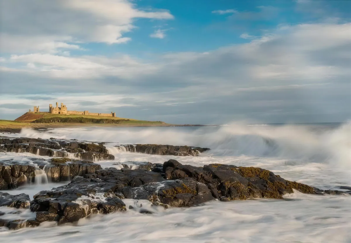 Waves breaking white over the rocks below Dunstanburgh Castle